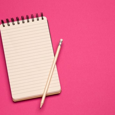 Spiral notebook and pencil on pink background"r